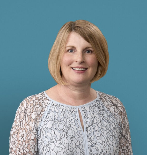 Professional headshot of Melissa Cousins, APRN-CNP, smiling in white lace top against teal background.