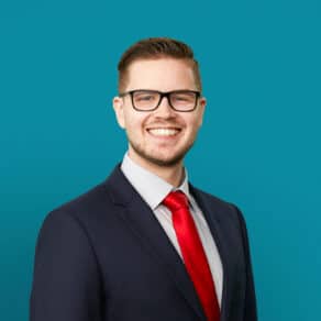 Professional headshot of Micah B. Schmal, DO in dark suit with red tie
