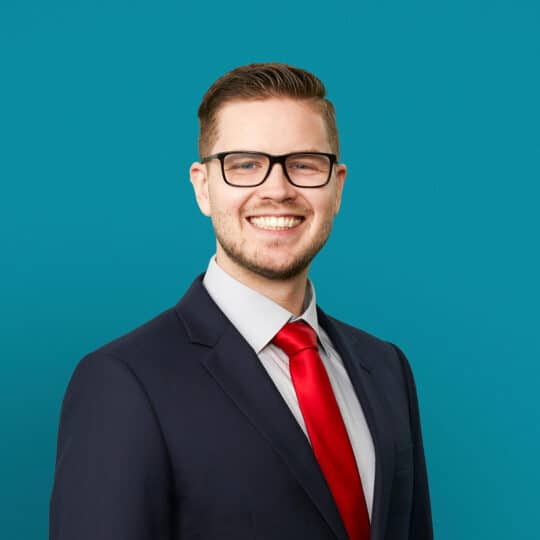 Professional headshot of Micah B. Schmal, DO in dark suit with red tie