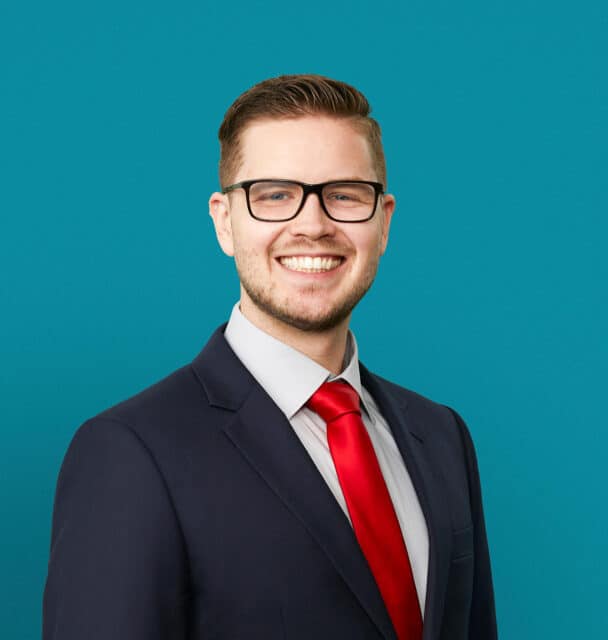 Professional headshot of Micah B. Schmal, DO in dark suit with red tie