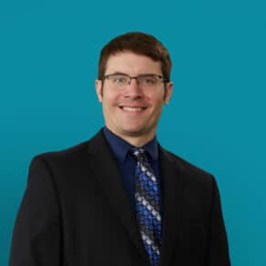 Professional headshot of Dr. Michael Jaje in dark suit against teal background