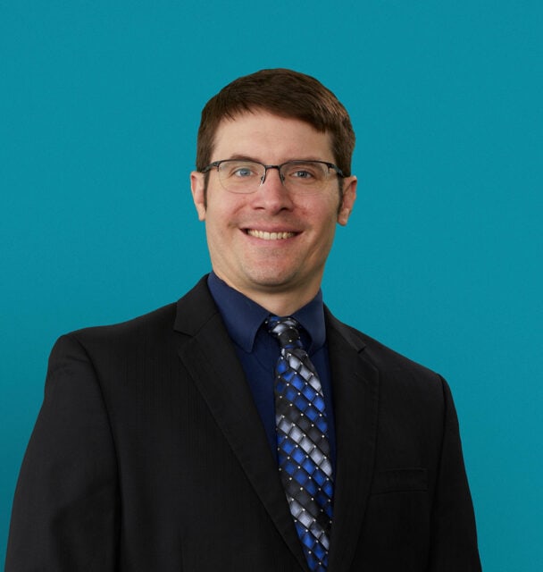 Professional headshot of Dr. Michael Jaje in dark suit against teal background