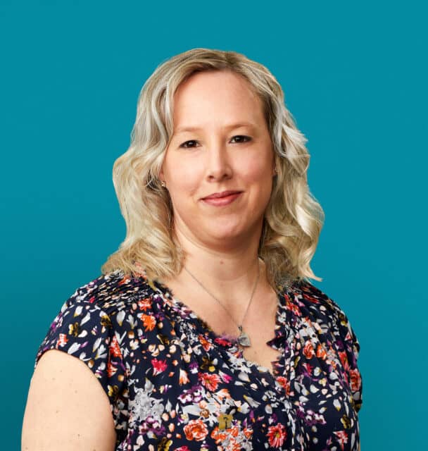 Professional headshot of Nicole "Nikki" Buckingham, APRN-CNP in floral top against teal background