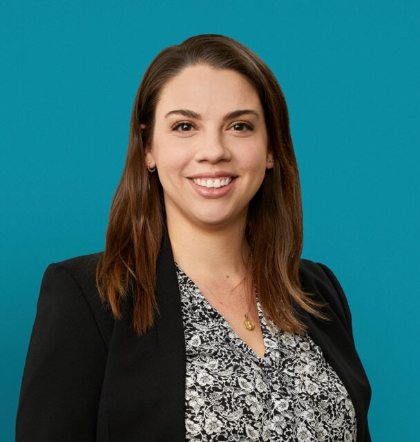 Professional headshot of Nicole Thomas, PharmD smiling in black blazer against teal background