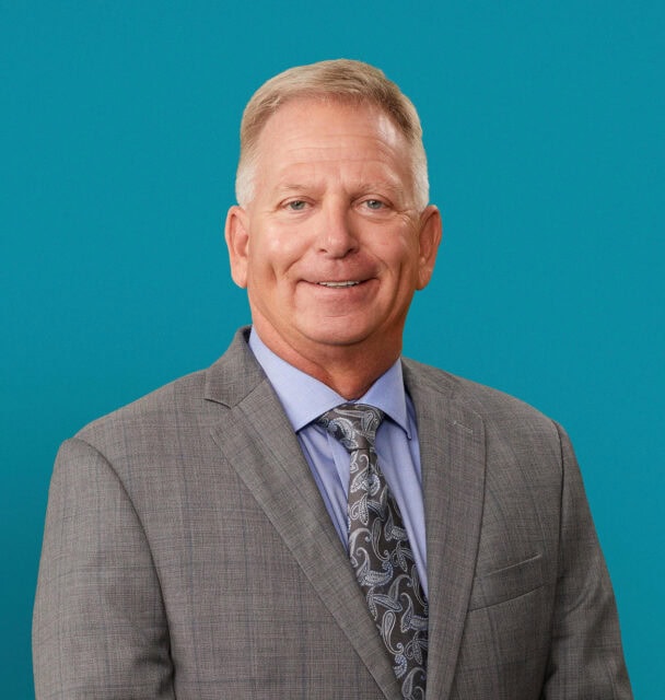 Professional headshot of Patrick J. Lytle, DO in gray suit against teal background