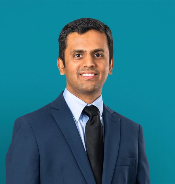 Professional headshot of Dr. Pratik M. Choksy in navy suit against teal background