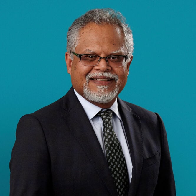 Professional headshot of Dr. Rajiva R. Singh in dark suit against teal background