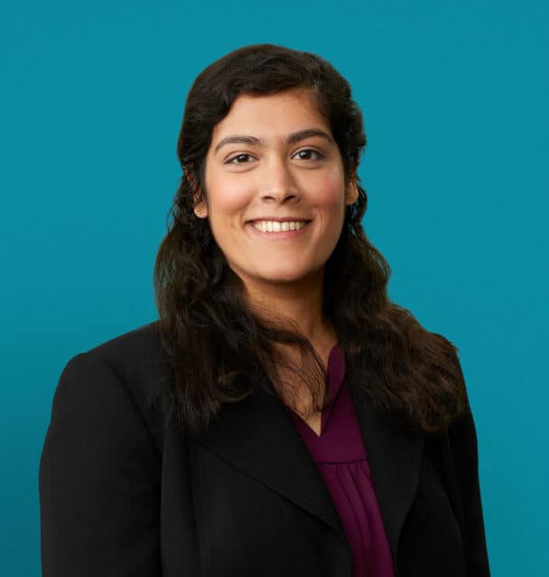 Professional headshot of Dr. Ramya Raghavan in black blazer against teal background