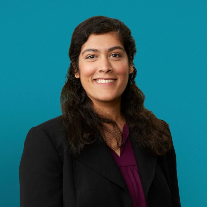 Professional headshot of Dr. Ramya Raghavan in black blazer against teal background