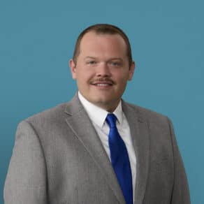 Professional headshot of Robert Henison, APRN-CNP in gray suit with blue tie
