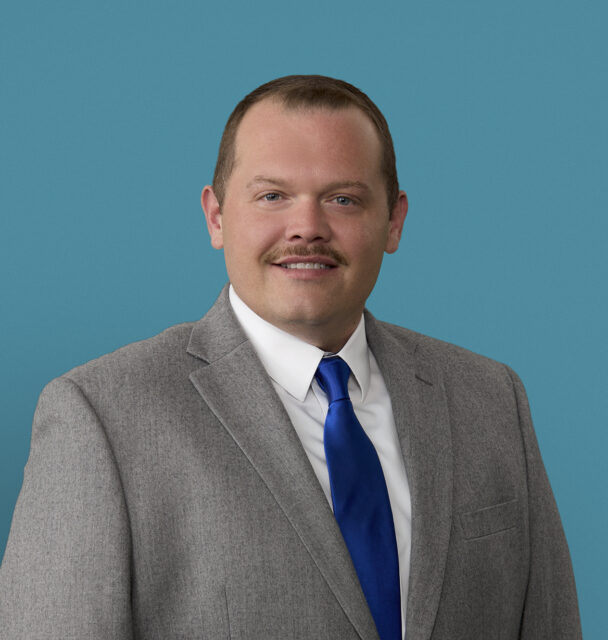 Professional headshot of Robert Henison, APRN-CNP in gray suit with blue tie