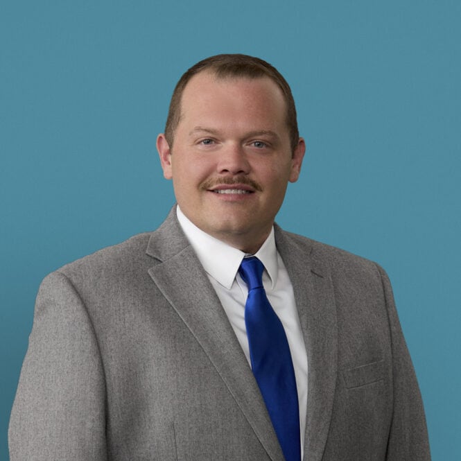 Professional headshot of Robert Henison, APRN-CNP in gray suit with blue tie