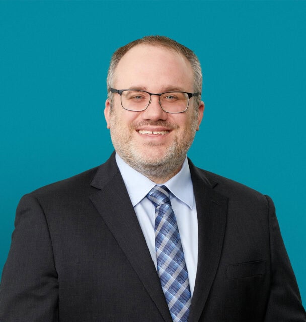 Professional headshot of Robert Polak, MD smiling in dark suit against teal background