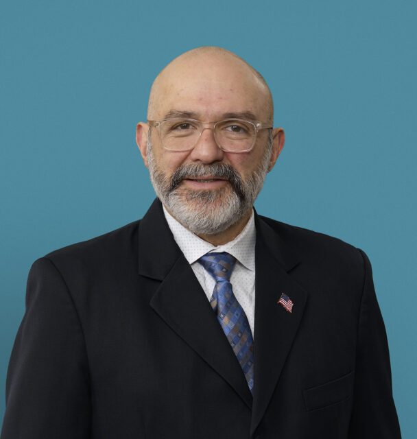 Professional headshot of Dr. Romel Garcia-Montilla in dark suit with blue tie