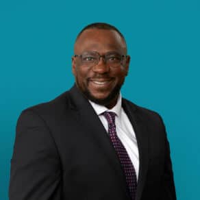 Professional headshot of Dr. Rory Lewis in dark suit and tie against teal background