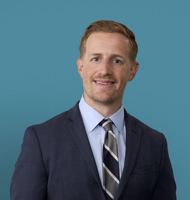 Professional headshot of Dr. Sam Keltner in dark suit against teal background