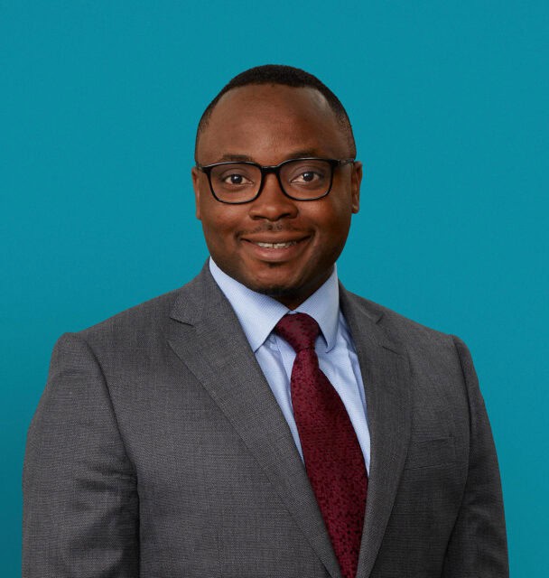 Professional headshot of Dr. Samson Alliu in gray suit with burgundy tie