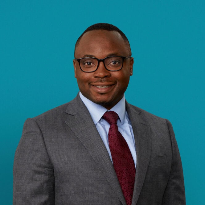 Professional headshot of Dr. Samson Alliu in gray suit with burgundy tie