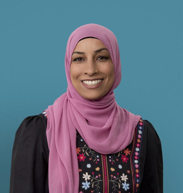 Professional headshot of Sarah Abdallah, PA-C, wearing pink hijab and embroidered black top, smiling warmly.