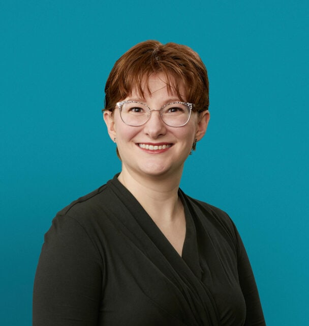 Professional headshot of Dr. Sarah Sample-Eppinger wearing glasses and dark top against teal background