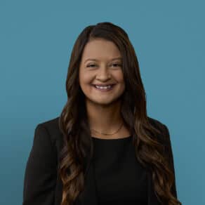 Professional headshot of Dr. Shaigan Bhatti smiling in black blazer against blue background