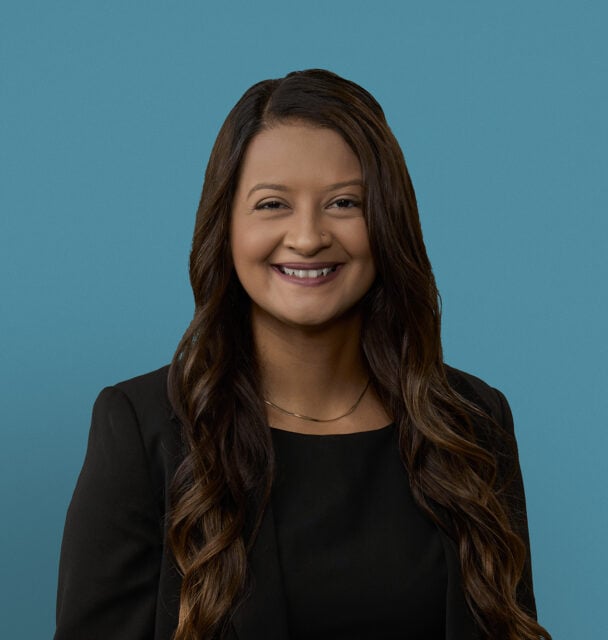 Professional headshot of Dr. Shaigan Bhatti smiling in black blazer against blue background