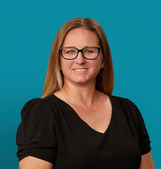 Professional headshot of Shannon Lewis, APRN-CNP, smiling in black top against teal background.