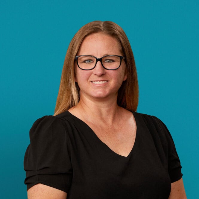 Professional headshot of Shannon Lewis, APRN-CNP, smiling in black top against teal background.
