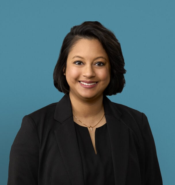 Professional headshot of Dr. Sonia Masih in black blazer against blue background