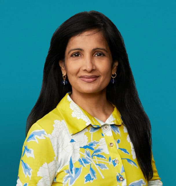 Professional headshot of Dr. Sunita M. Reddy wearing yellow floral shirt against teal background