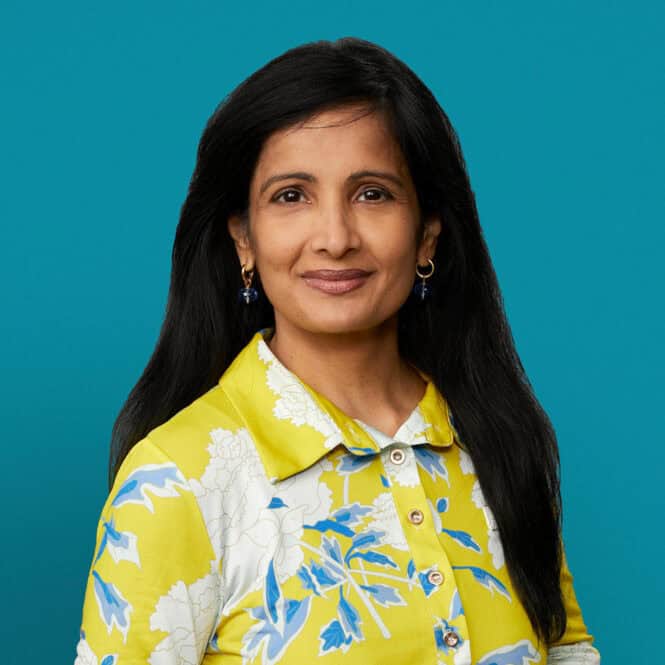 Professional headshot of Dr. Sunita M. Reddy wearing yellow floral shirt against teal background