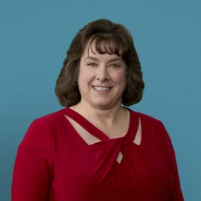 Professional headshot of Teresa VanHoose, APRN-CNP in red top against blue background