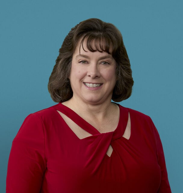 Professional headshot of Teresa VanHoose, APRN-CNP in red top against blue background