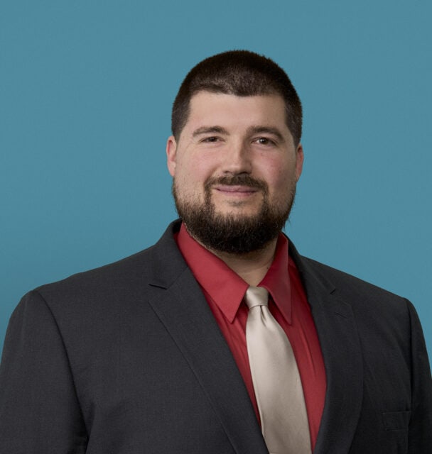 Professional headshot of Tyler Peckham, LPCC in dark suit with red shirt and beige tie