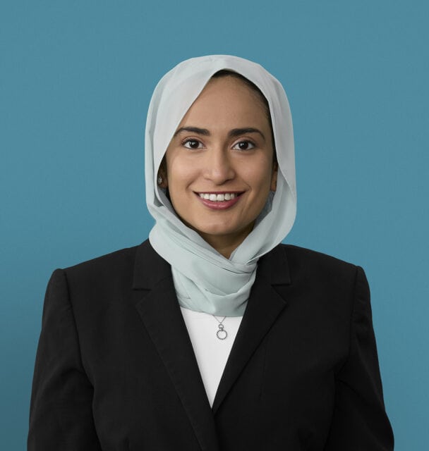 Professional headshot of Dr. We'am Hussain wearing hijab and dark business suit