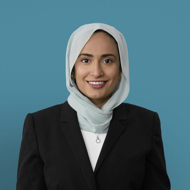 Professional headshot of Dr. We'am Hussain wearing hijab and dark business suit
