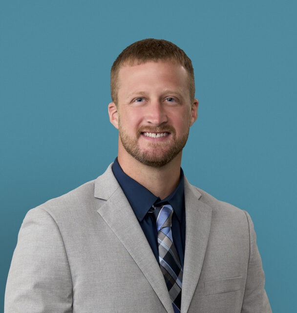 Professional headshot of Zachariah P. Zehler, APRN-CNP in light gray suit and tie