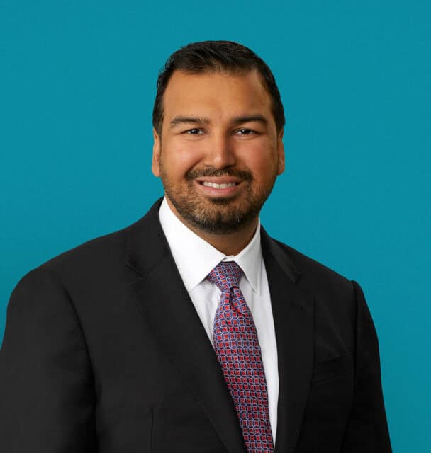 Professional headshot of Dr. Zubin Agarwal in dark suit against turquoise background