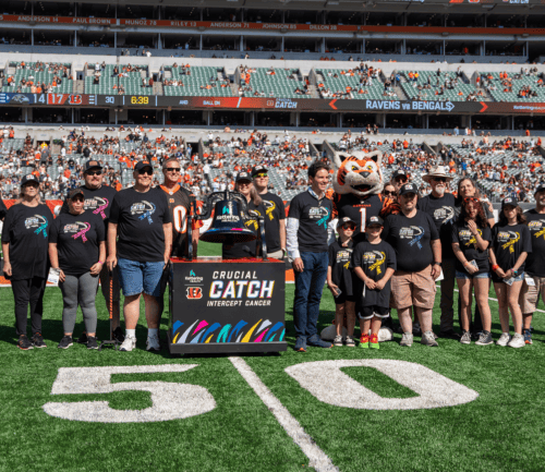 Group of families posing on football field with Crucial Catch cancer awareness banner