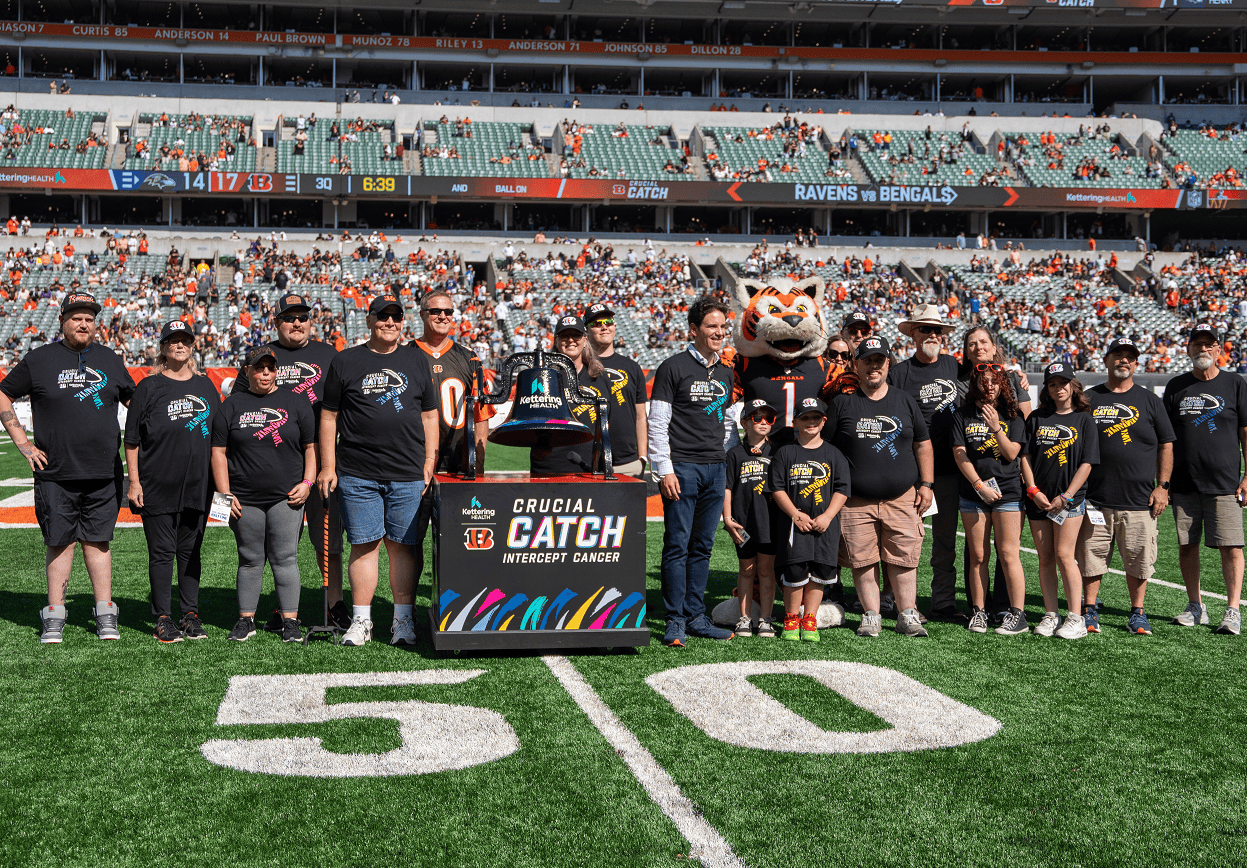 Group of families posing on football field with Crucial Catch cancer awareness banner