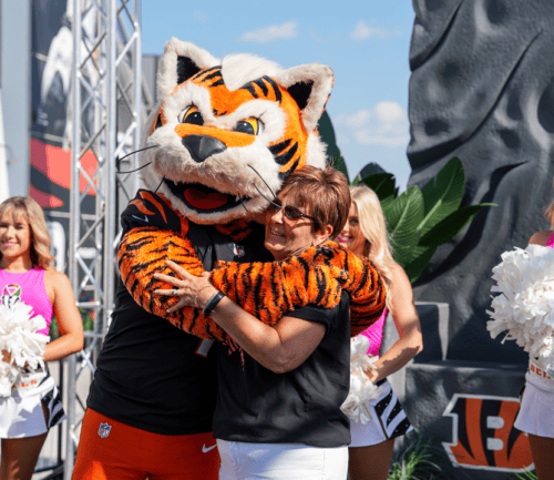 Cincinnati Bengals mascot hugging woman surrounded by cheerleaders with pom-poms