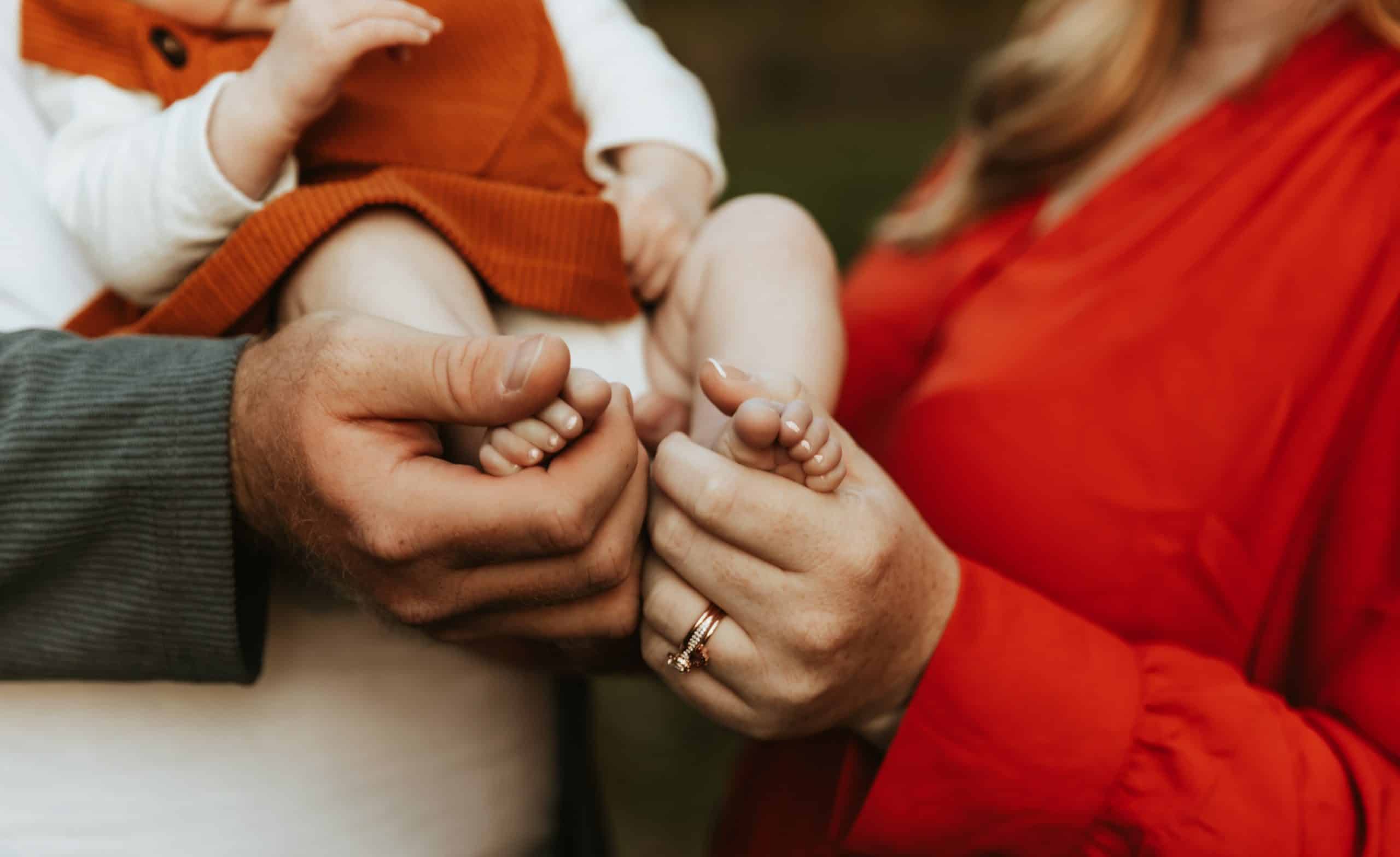 Parents gently holding their baby's tiny feet in their hands