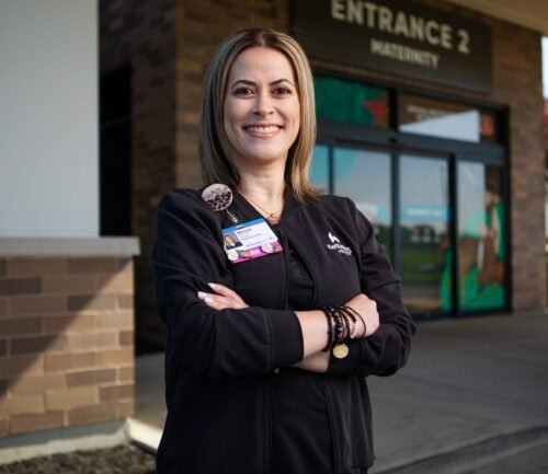 Healthcare professional in black scrubs with arms crossed standing outside medical facility entrance