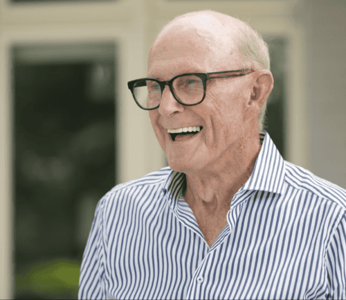 Smiling senior man with glasses in striped shirt outdoors at healthcare facility