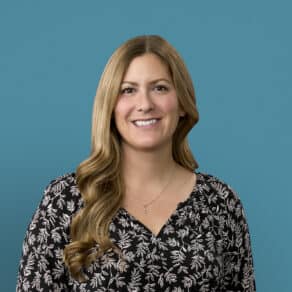Professional headshot of Kathryn Koble wearing black floral top against blue background