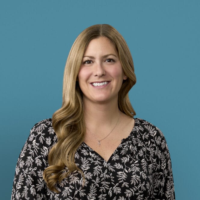 Professional headshot of Kathryn Koble wearing black floral top against blue background